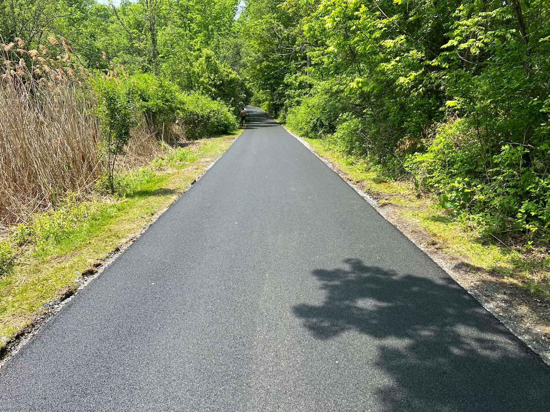 Freshly paved black asphalt driveway leading to a two-car garage with open doors.