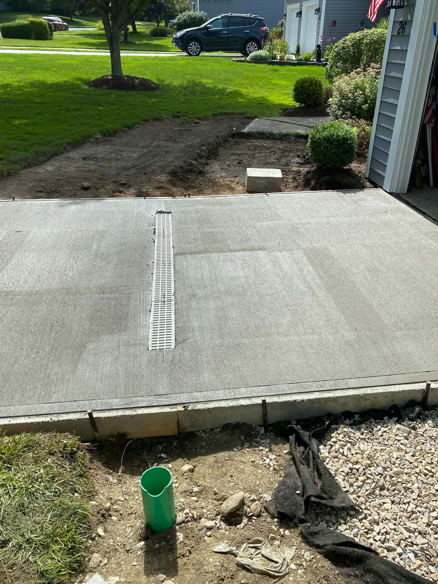 Driveway with concrete repair in progress; green pipe and gravel in foreground.