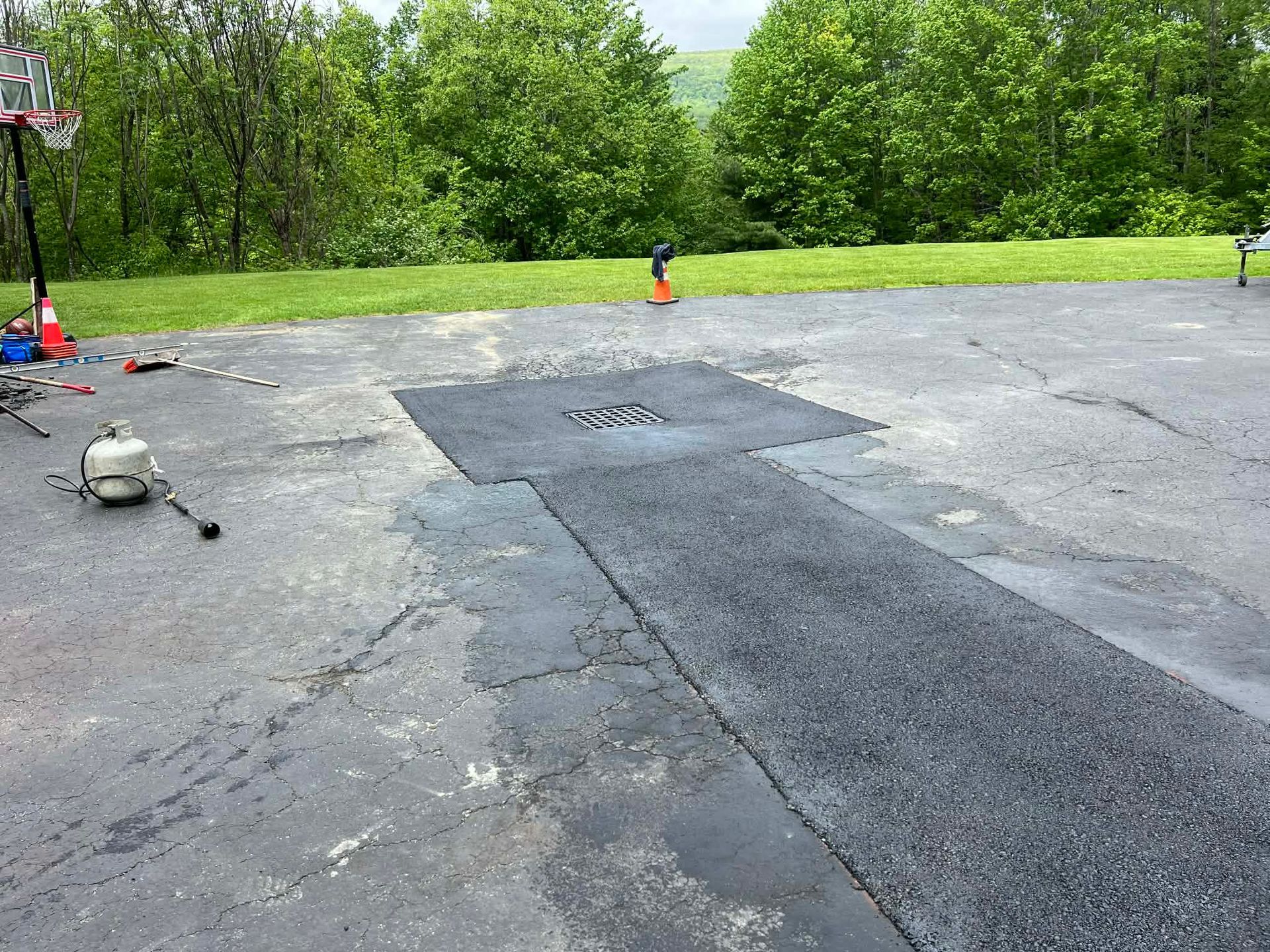 Asphalt driveway repair in progress; patch and newly laid asphalt visible.