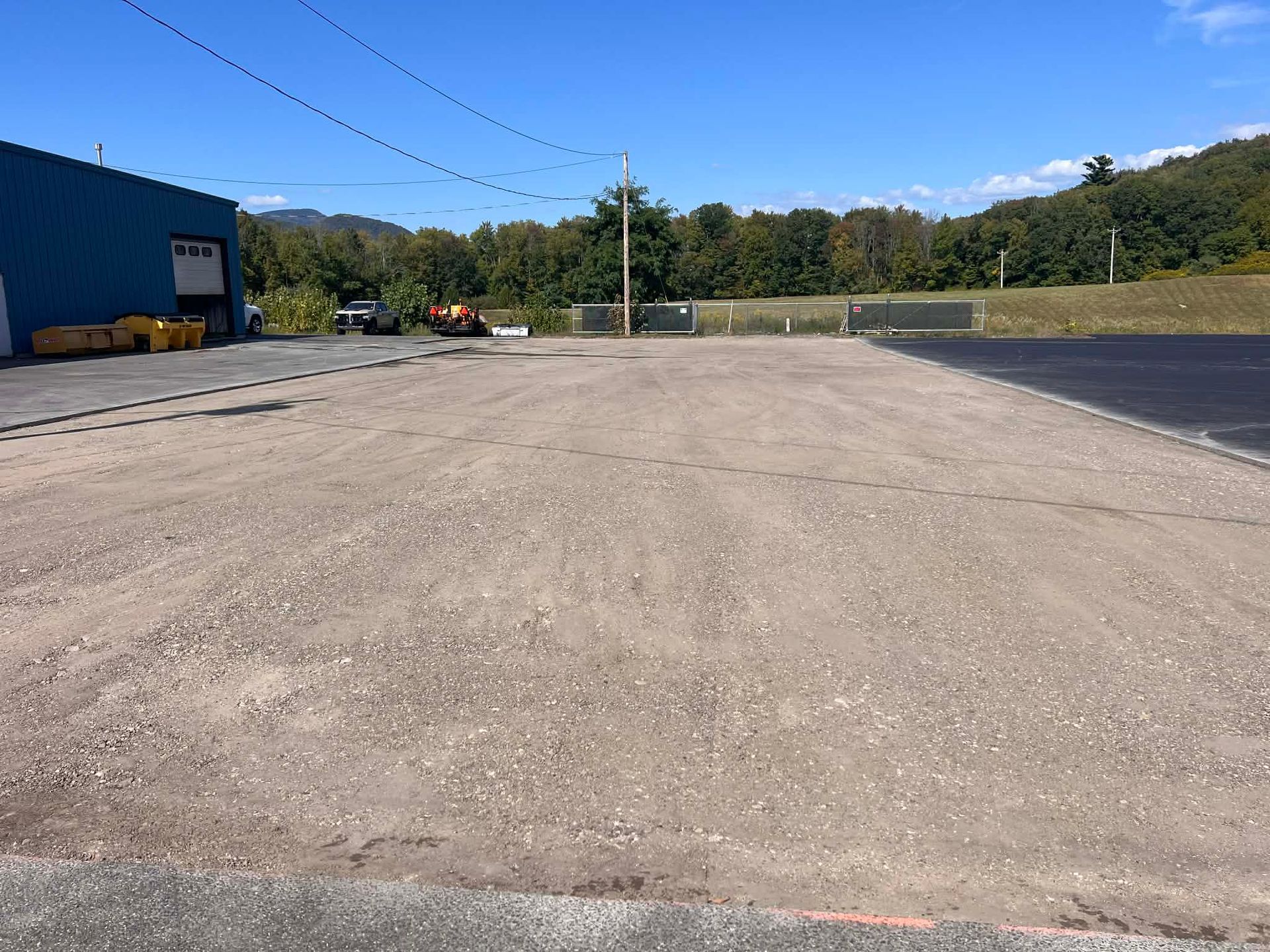 Gravel-covered lot next to a blue building with trees and clear sky in the background.