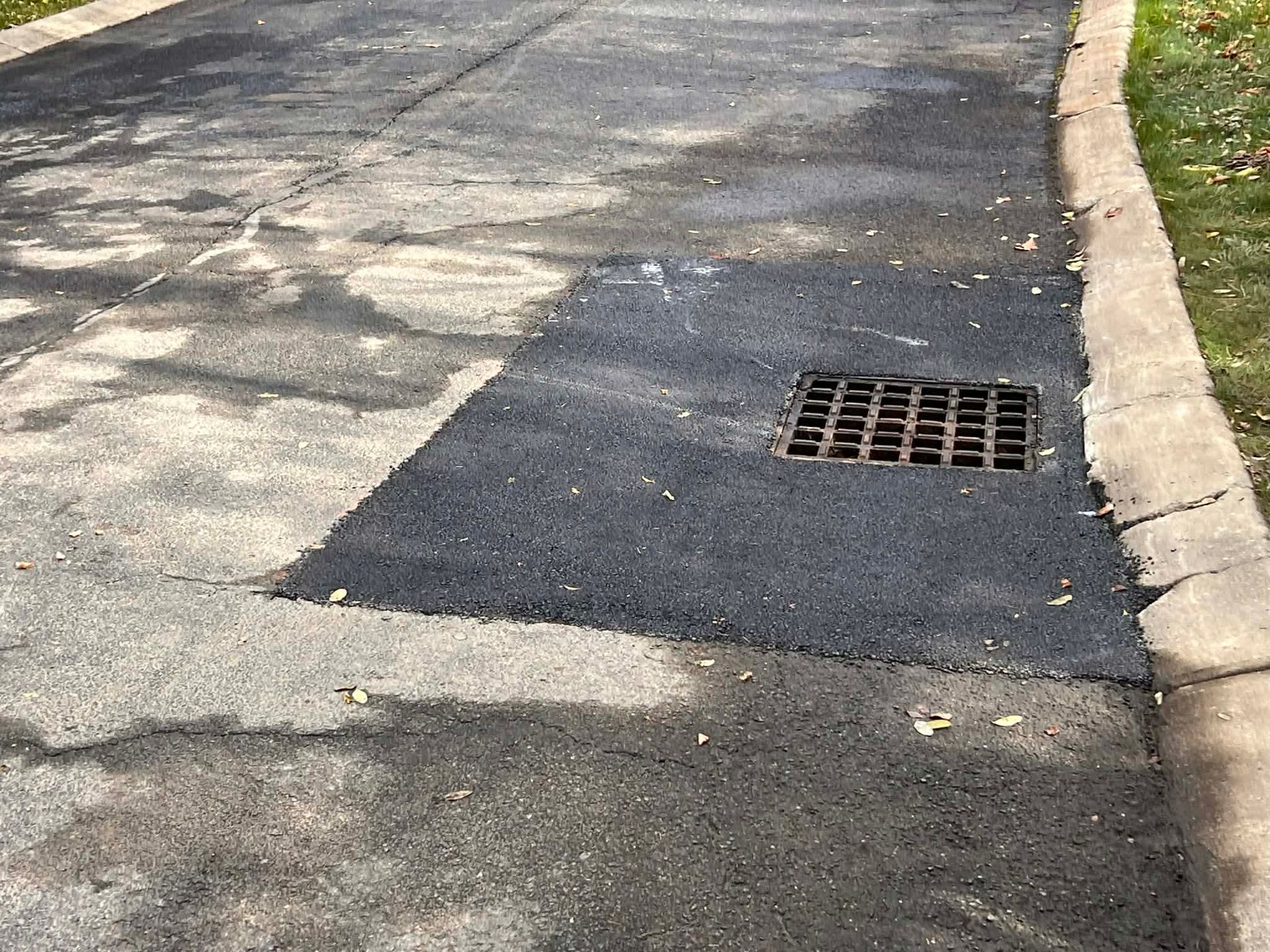 Asphalt driveway with a rectangular patch around a drain.