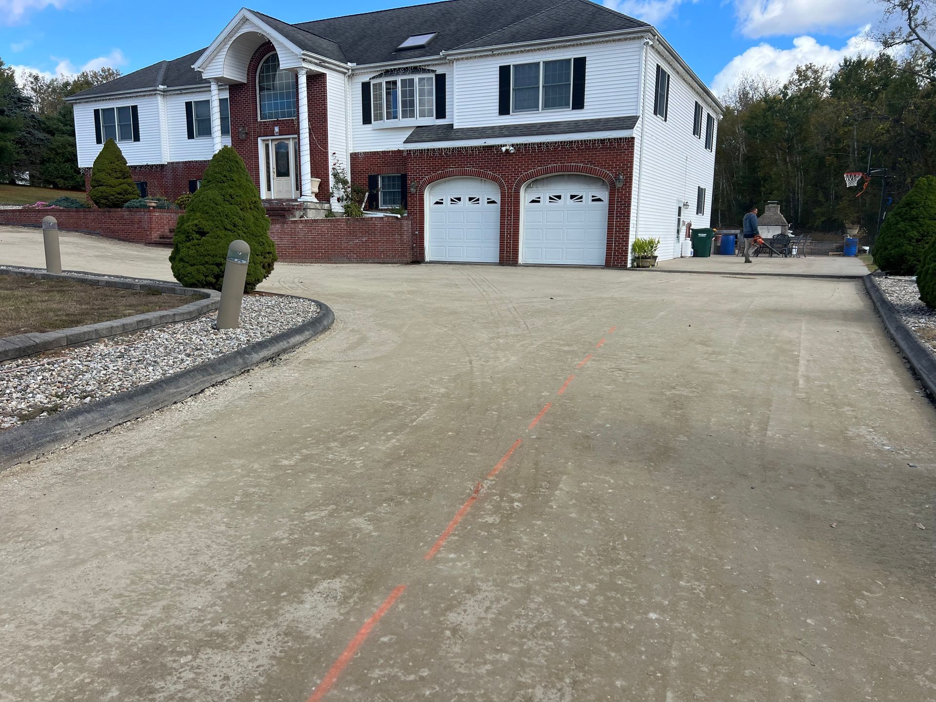 Two-story house with a large gravel driveway. Red brick accent, white garage doors.