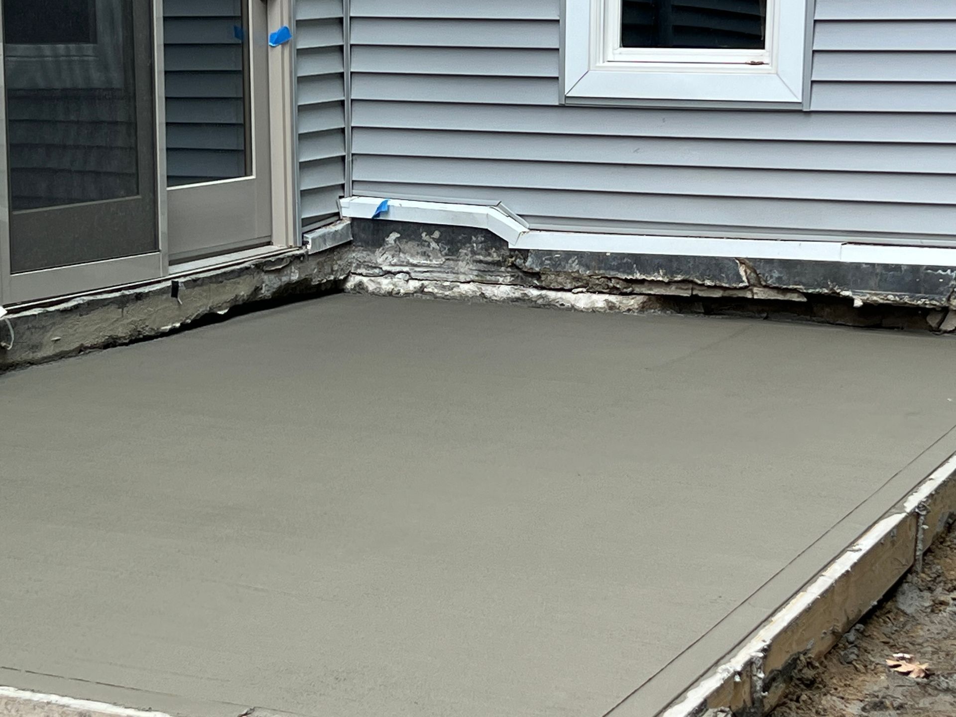 Newly poured concrete patio next to a blue-gray house with a window and door.