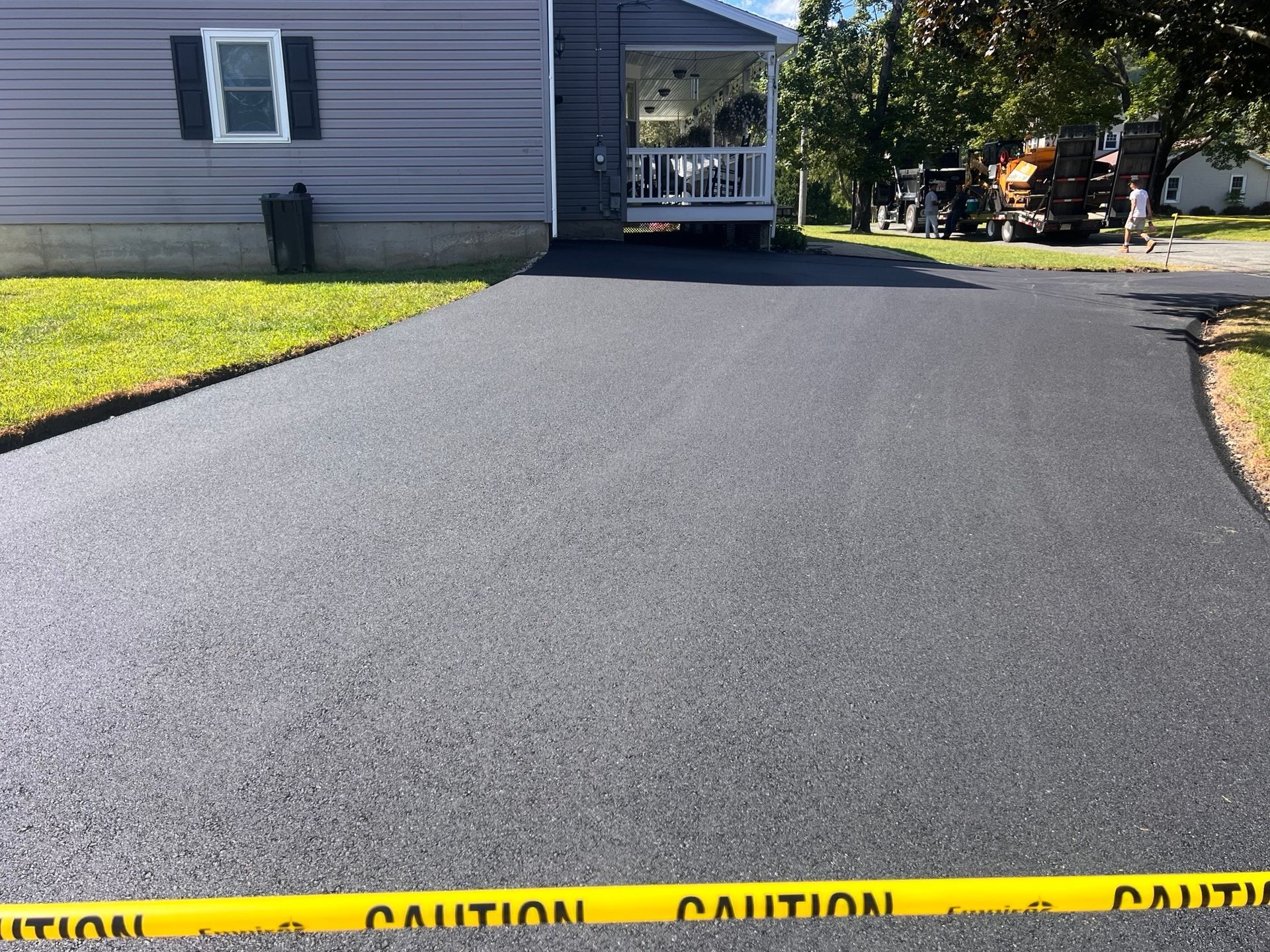 Newly paved asphalt driveway in front of a gray house, caution tape in the foreground.