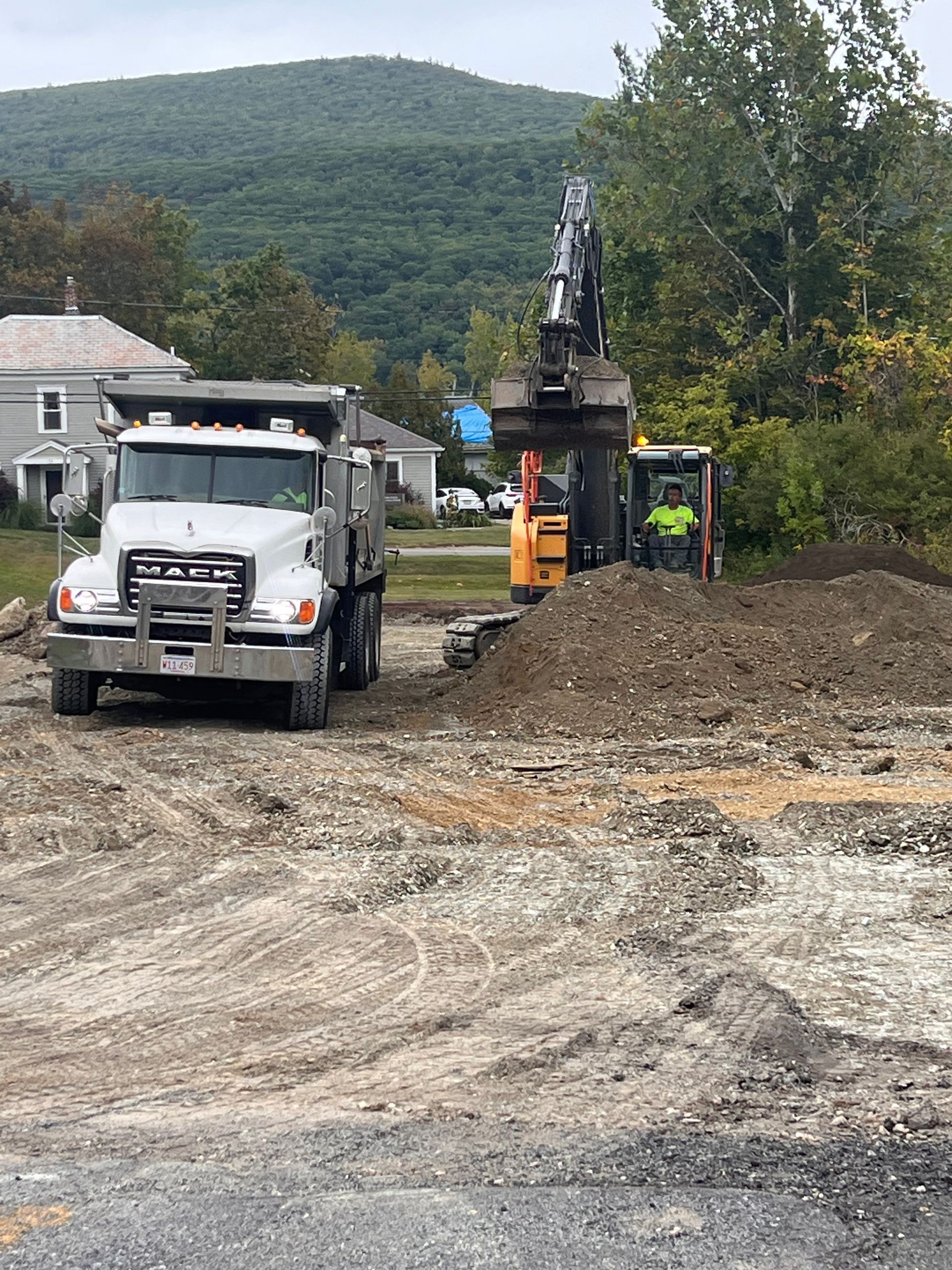 Construction site: Dump truck, excavator, small digger working on the land with a mountain in the background.