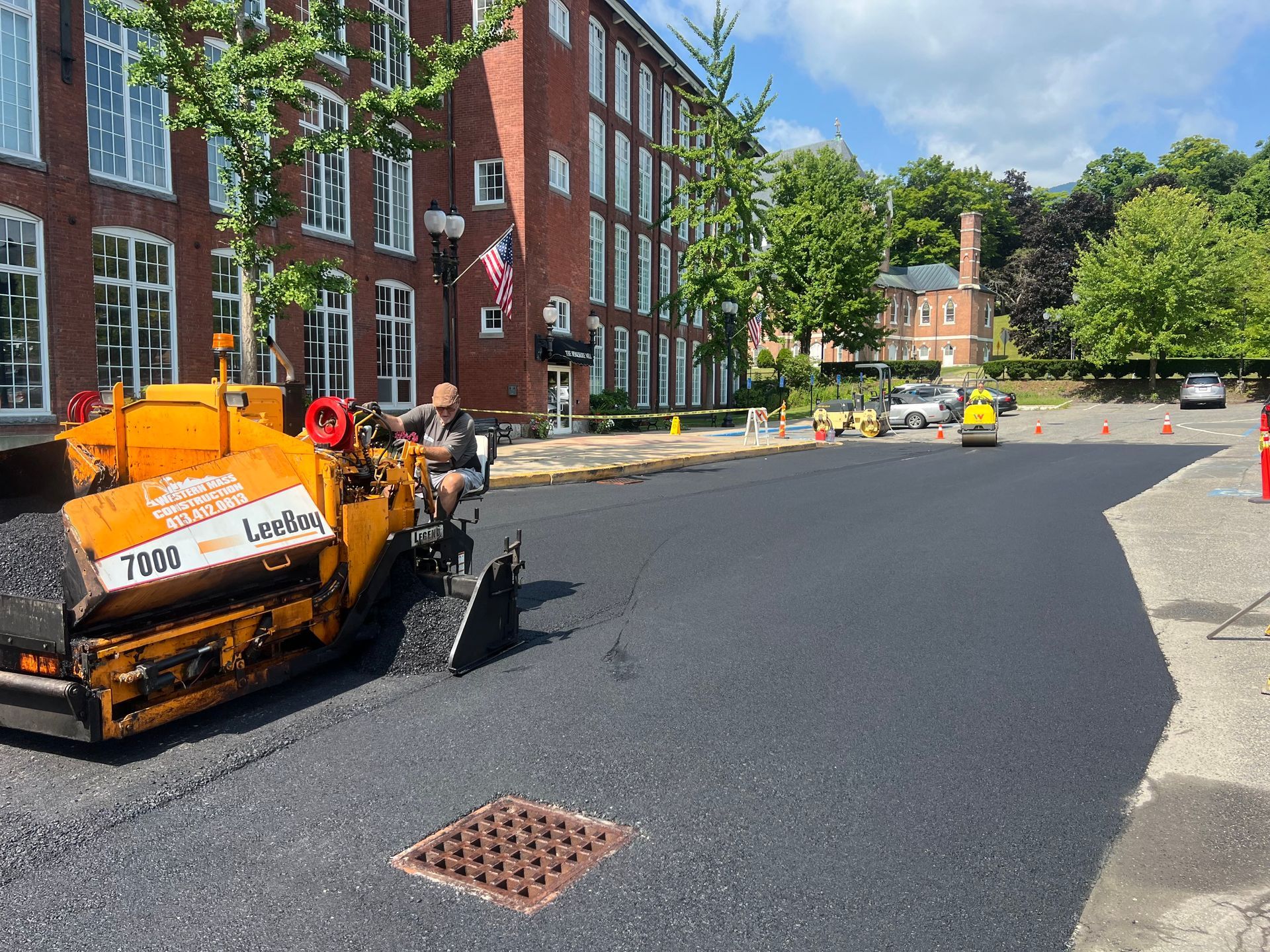 Asphalt paving machine laying new black asphalt on street in front of brick building.