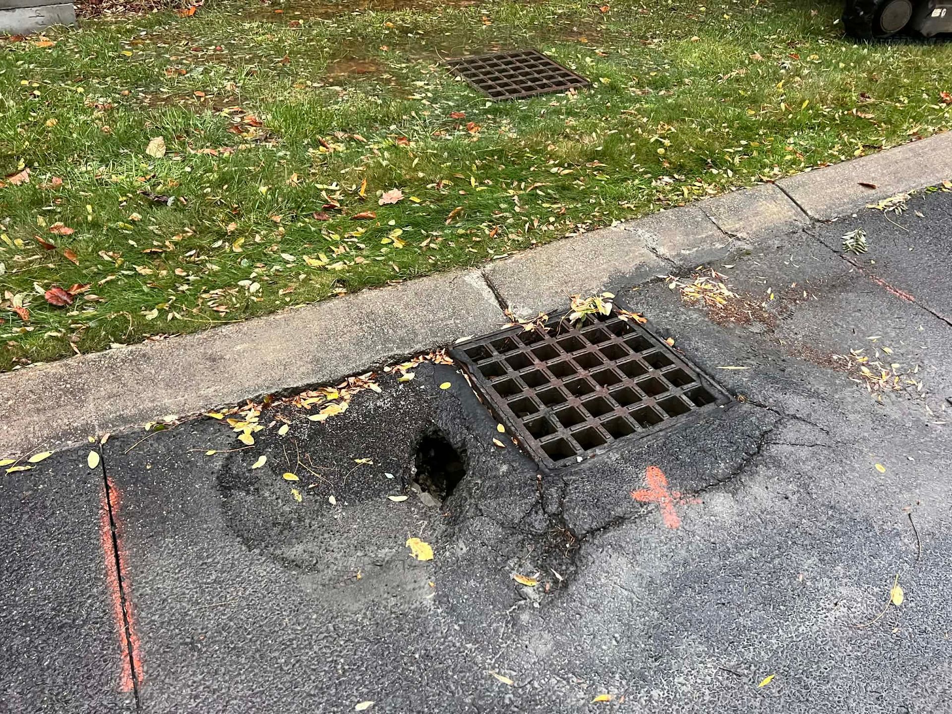 Damaged asphalt with a missing section next to a storm drain.