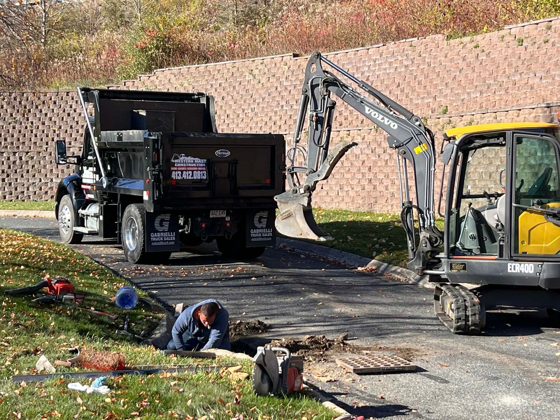 Construction site with a dump truck, excavator, and worker inspecting a sewer grate.