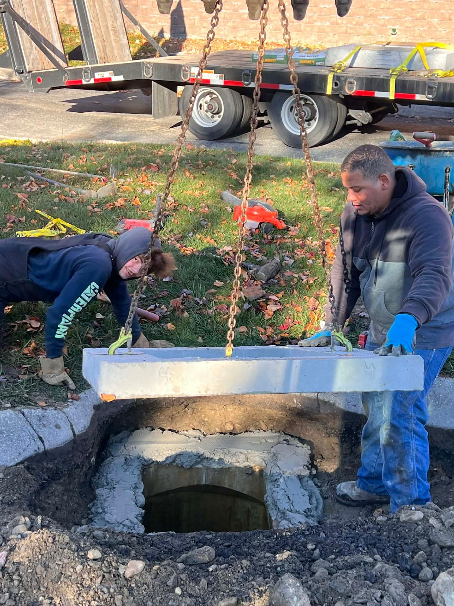Two workers lowering a stone slab onto a concrete structure with a chain hoist outdoors.