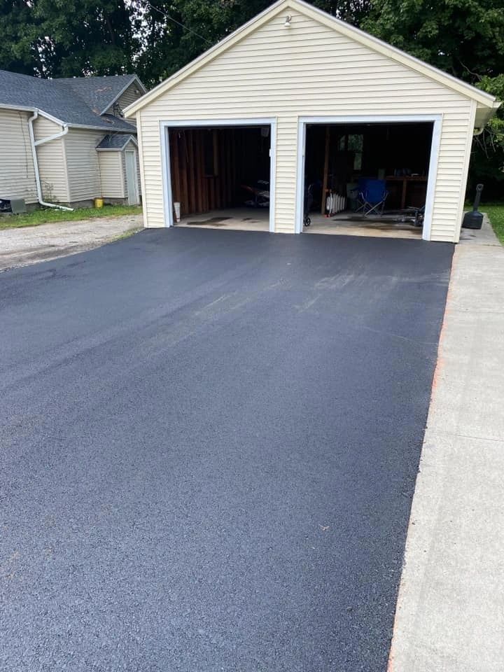 Freshly paved black asphalt driveway leading to a two-car garage with open doors.