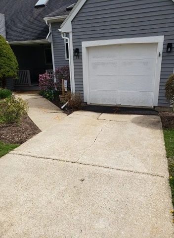 Concrete driveway leads to a garage. The house has gray siding and landscaping on either side of the driveway.
