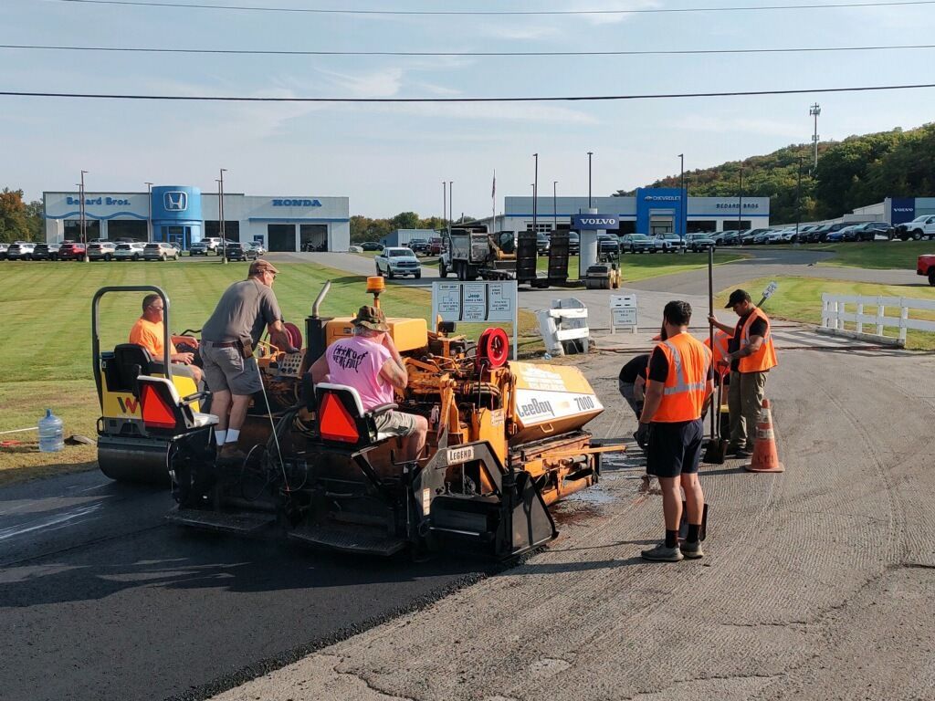 Road paving crew working, near a car dealership, asphalt machine laying new road.
