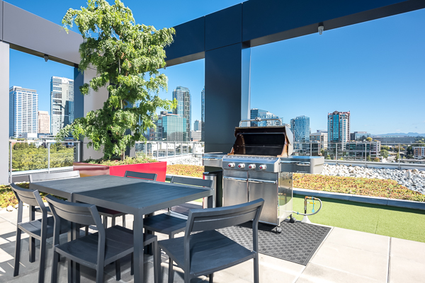 Photo of a seating area atop the rooftop lounge, near a barbecue grill and with the buildings in the back