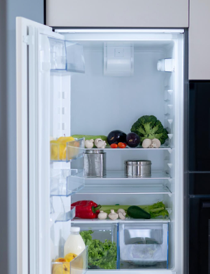 Refrigerador abierto lleno de productos: brócoli, berenjenas, pimientos y champiñones.