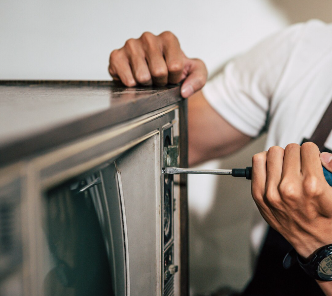 Persona que utiliza un destornillador para reparar un televisor antiguo.