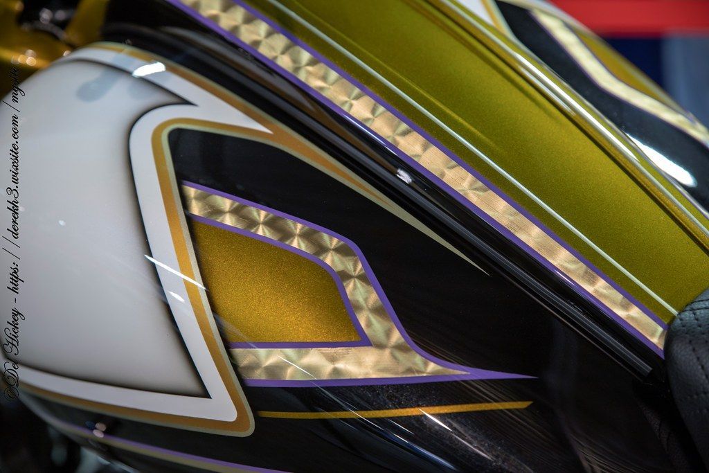 Een close-up van een motorfiets met gouden en paarse verf en bladgoud en pinstripe en parelmoer witverf