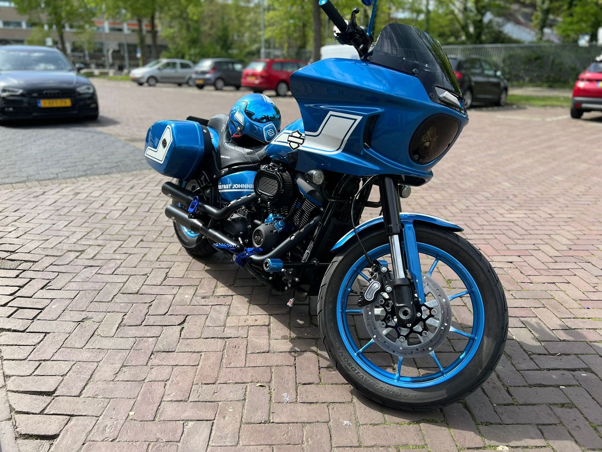 Een blauwe Harley Davidson motorfiets met bijpassende helm staat geparkeerd op een stenen stoep.