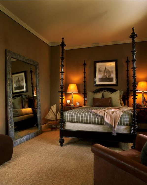 Warm bedroom with a canopy bed, bedside lamps, large mirror, and beige carpet.
