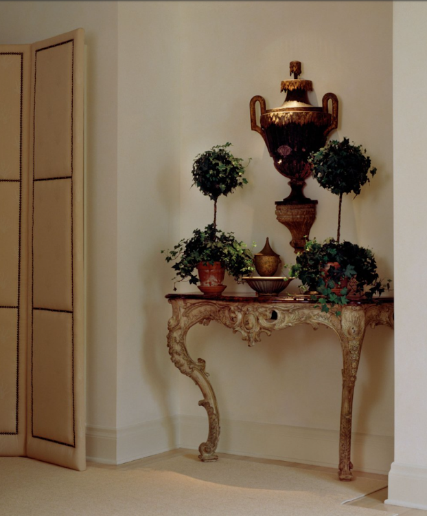 Decorative console table with potted plants and a large urn in a beige room