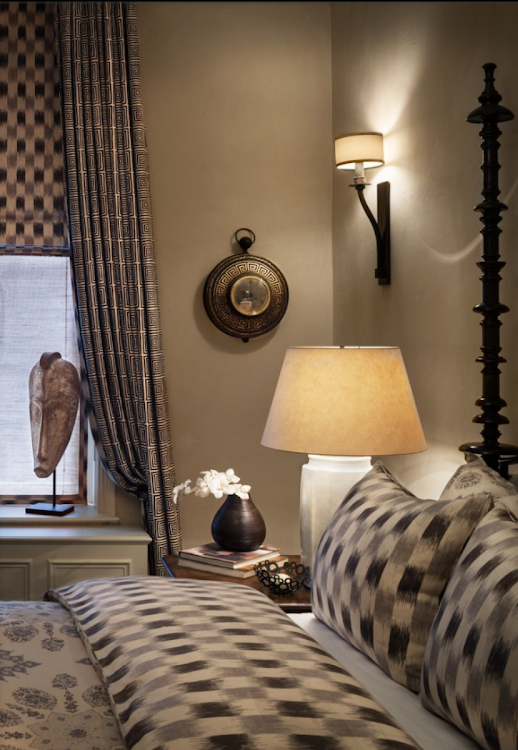 Cozy bedroom with checkered bedding, bedside lamp, wall sconce, and window with curtains