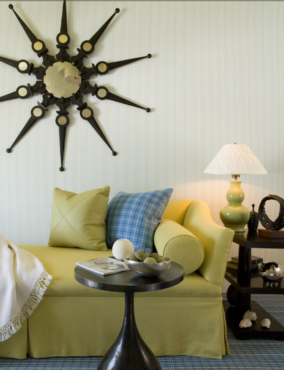 Yellow sofa with patterned pillows, black side table, lamp, and sunburst wall decor in a cozy living room