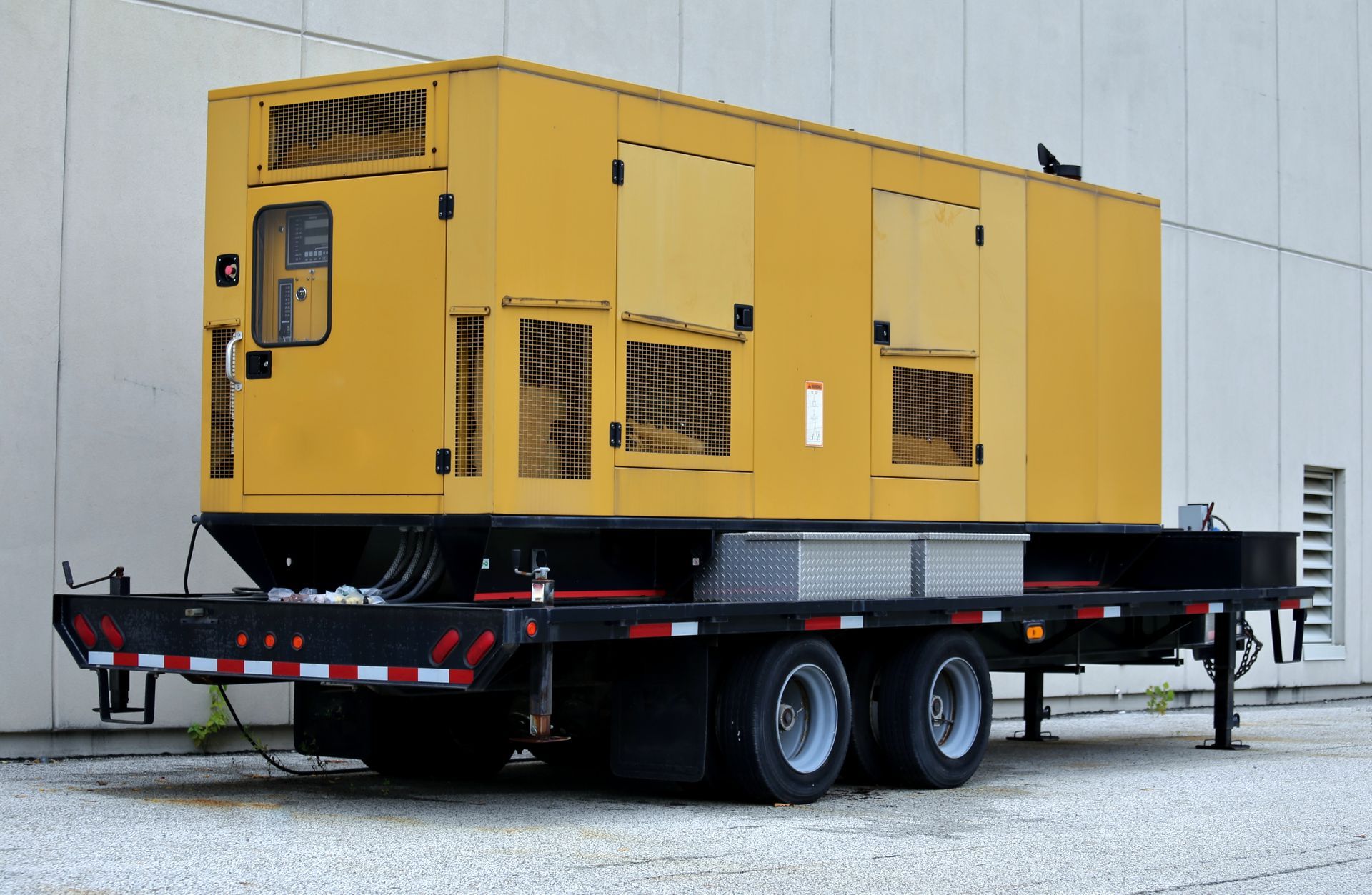 A large yellow generator is on a trailer in front of a building