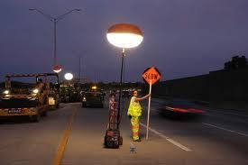 A woman is standing on the side of a highway holding a slow sign.