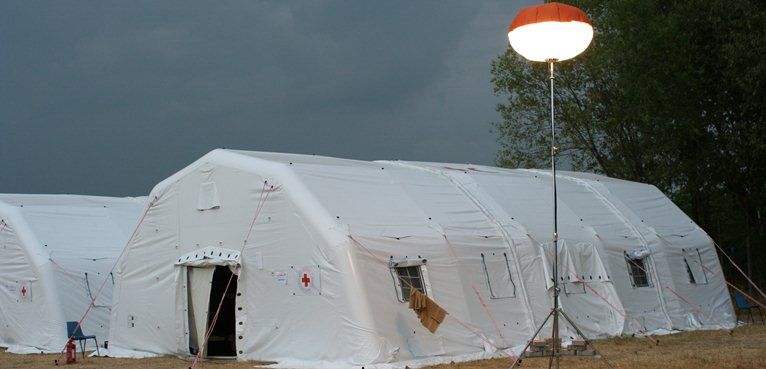 A group of tents are sitting in a field with a light hanging from a pole in front of them.