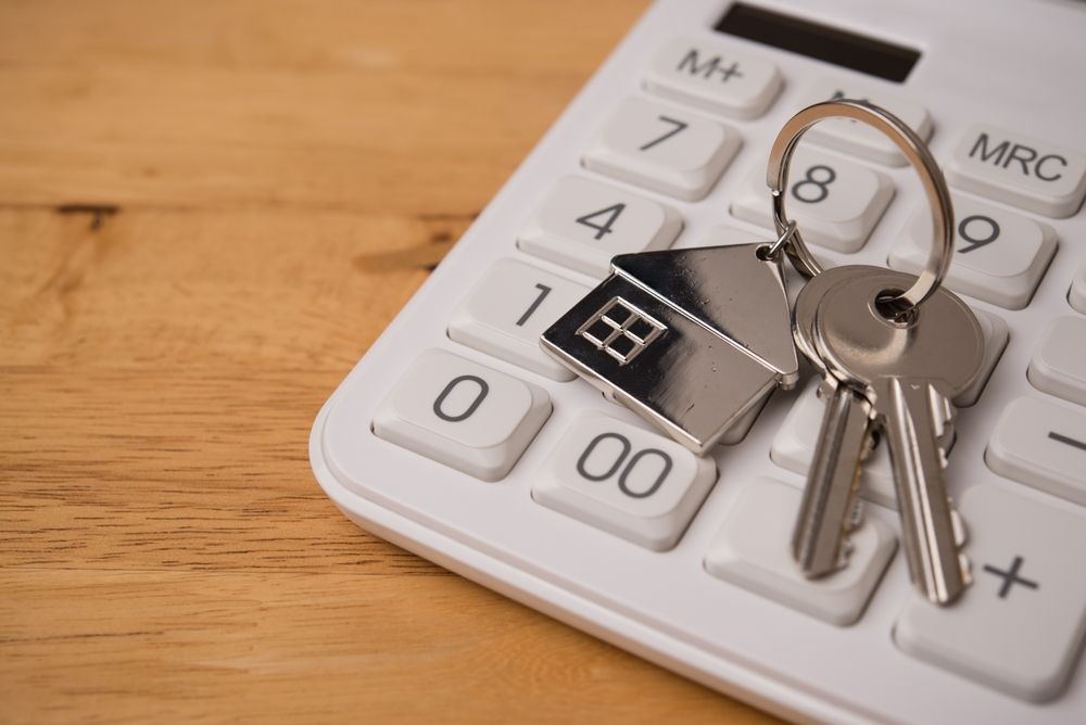 Keys with a house-shaped charm resting on a white calculator, on a wooden surface.