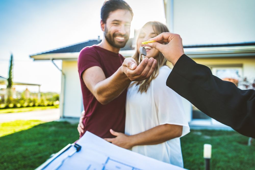 Couple receiving house keys from a person, standing in front of their new home.