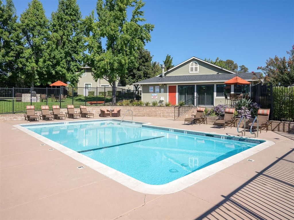 Outdoor community pool with lounge chairs and a pool building in the background.