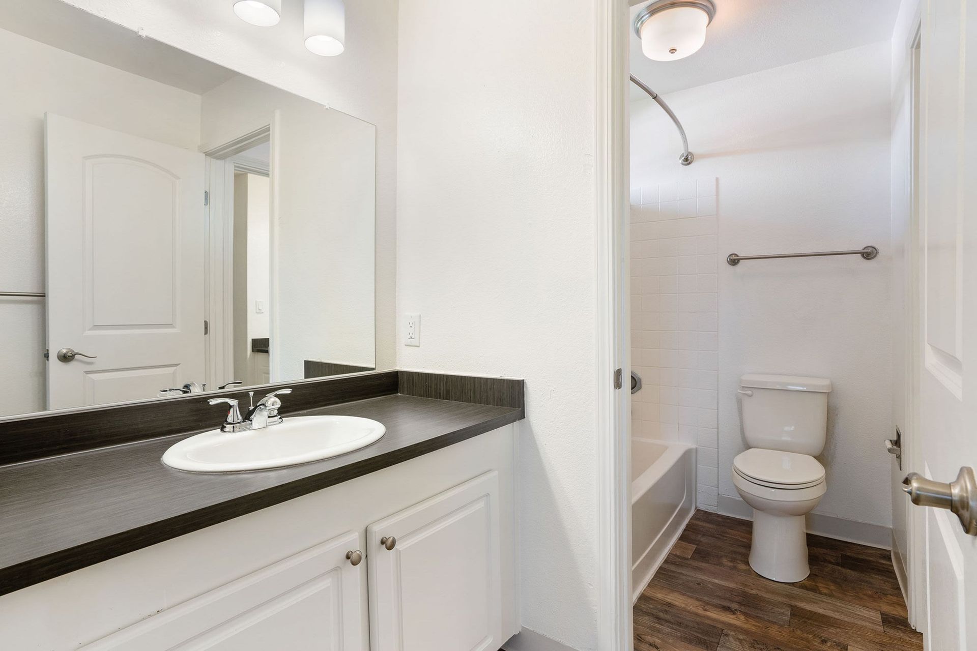 Bathroom with white walls, vanity, toilet, and a shower/tub combo with wood-look flooring.