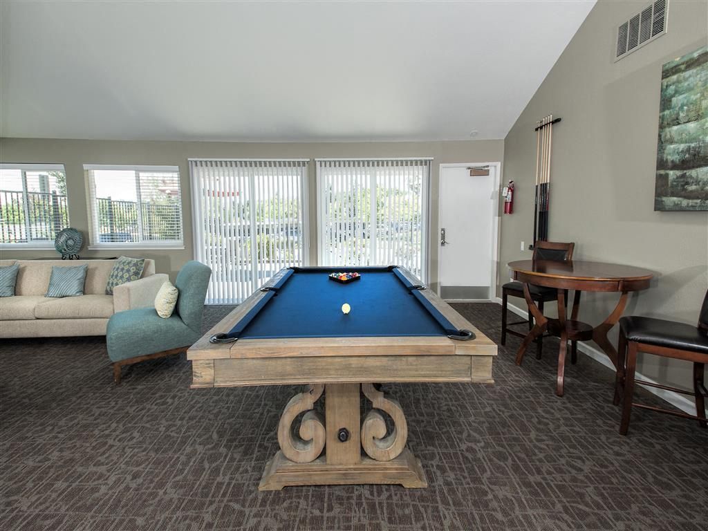 Indoor community recreation room with a pool table, sofa seating, and large windows.
