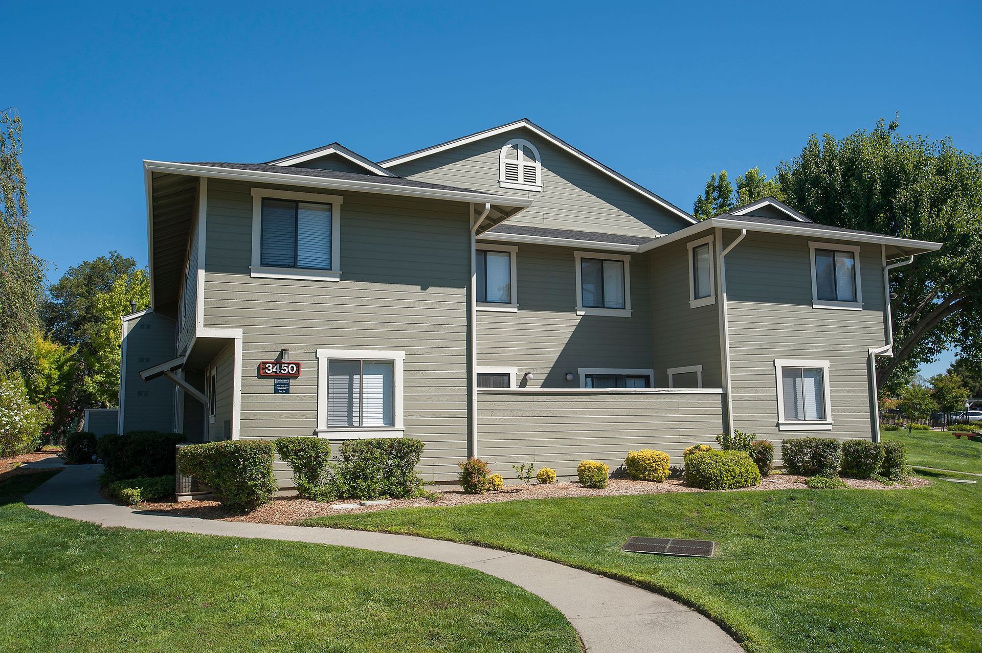 Two-story apartment building with green siding and a walkway in front, under a blue sky.