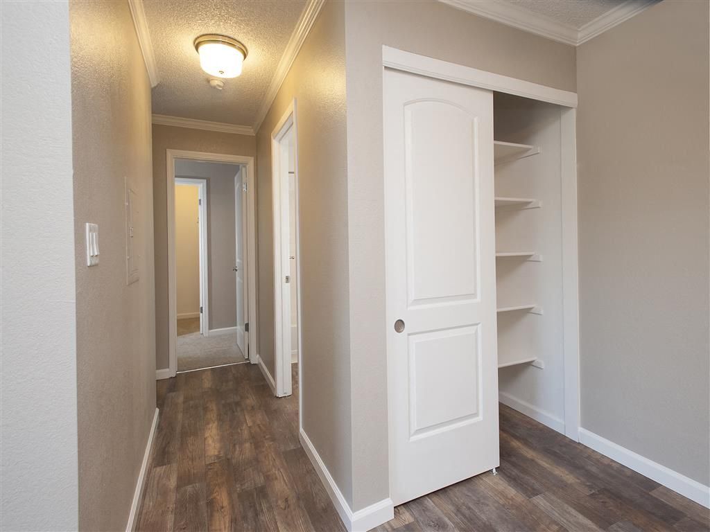 Hallway inside an apartment showing a white closet with shelves and wood-look flooring.