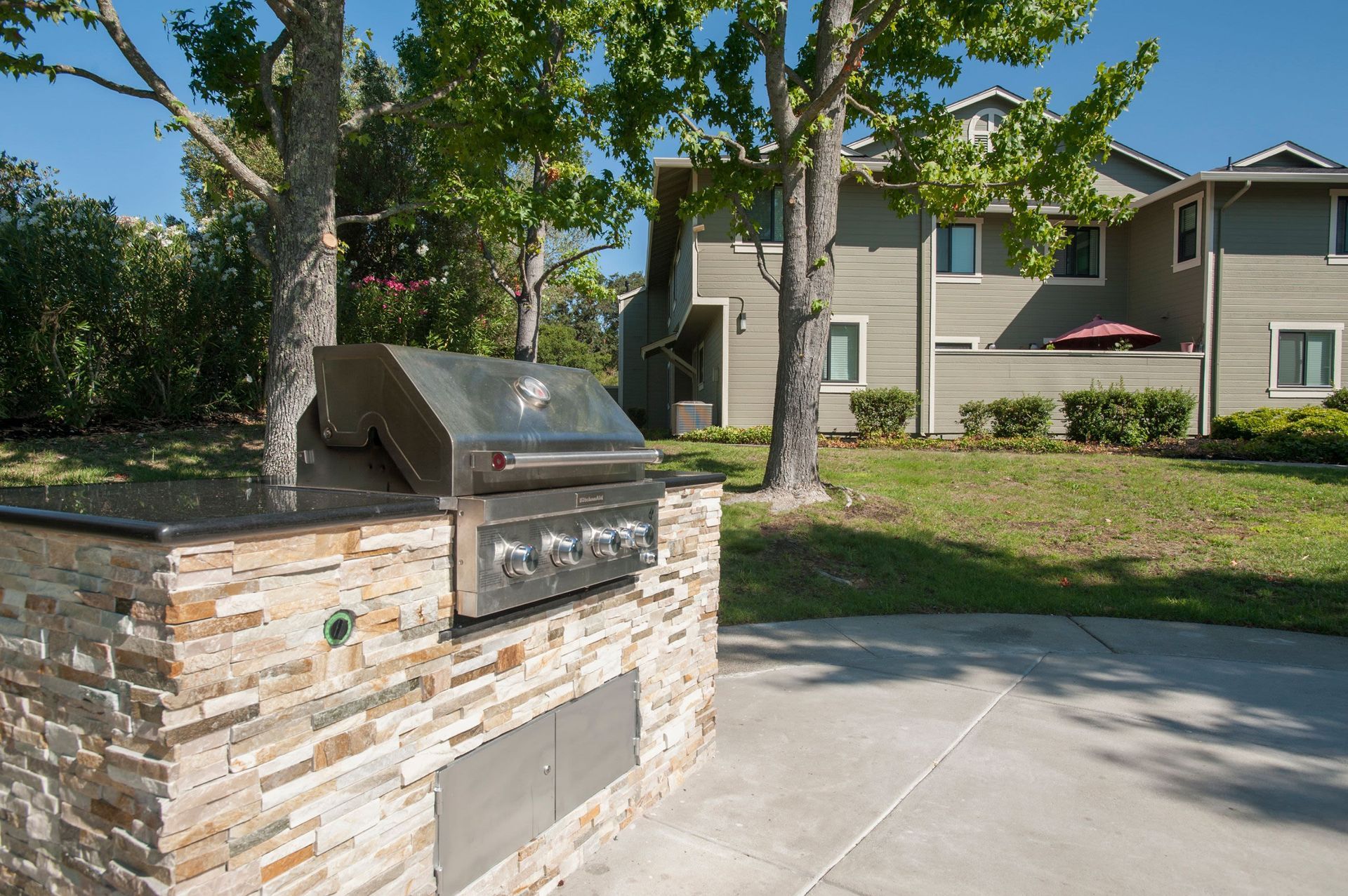 Outdoor built-in grill with stone facade and a stainless steel grill top in front of an apartment building.