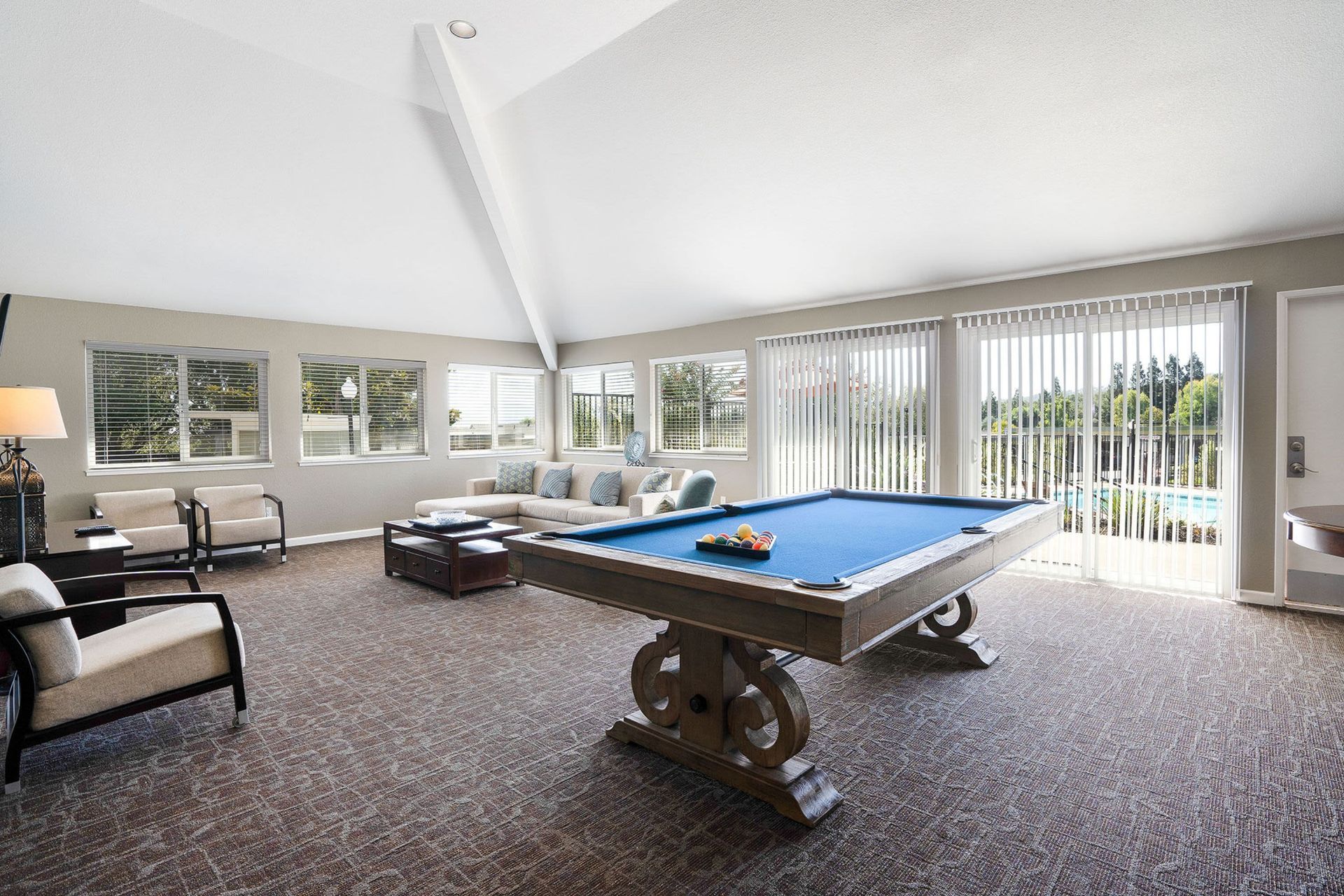 Game room with pool table, couches, windows, and neutral carpet.