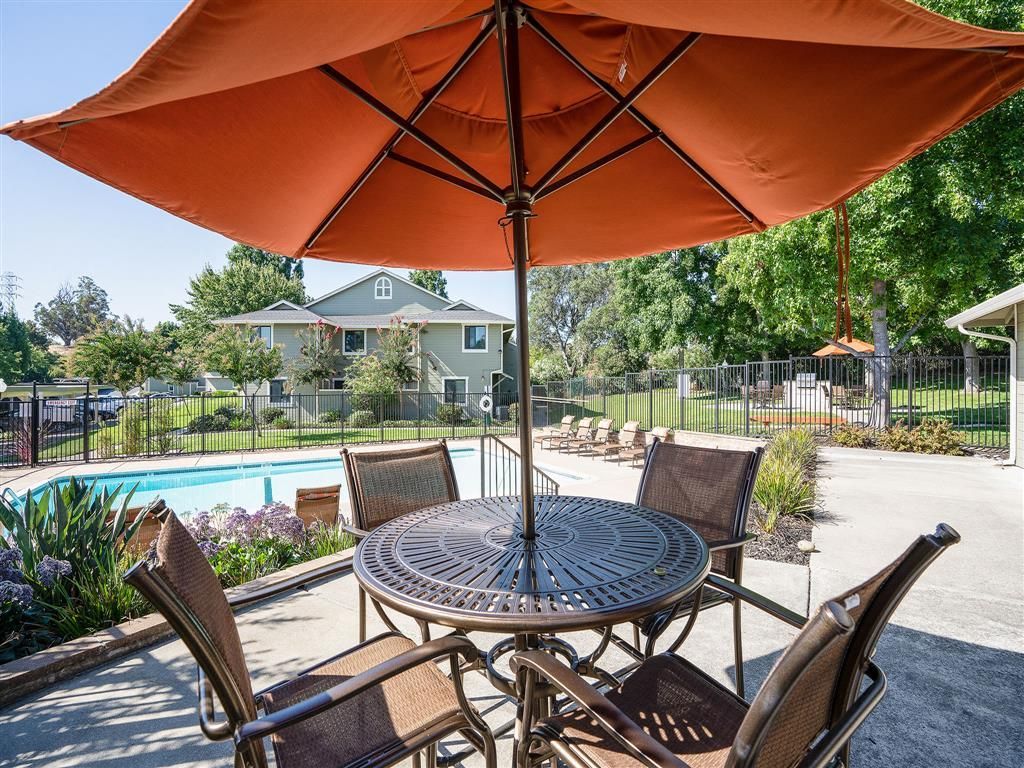 Outdoor pool area with a round table, chairs, and a large orange umbrella.