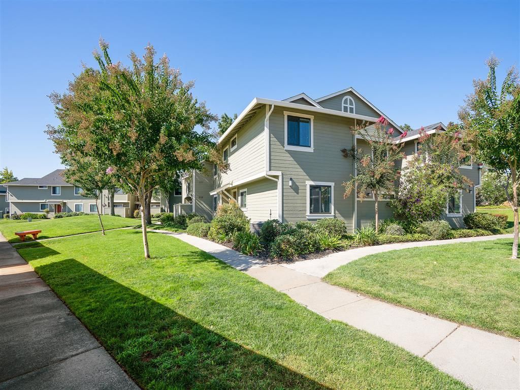 Exterior view of a multi-building apartment community with green lawns, trees, and curved walkways.