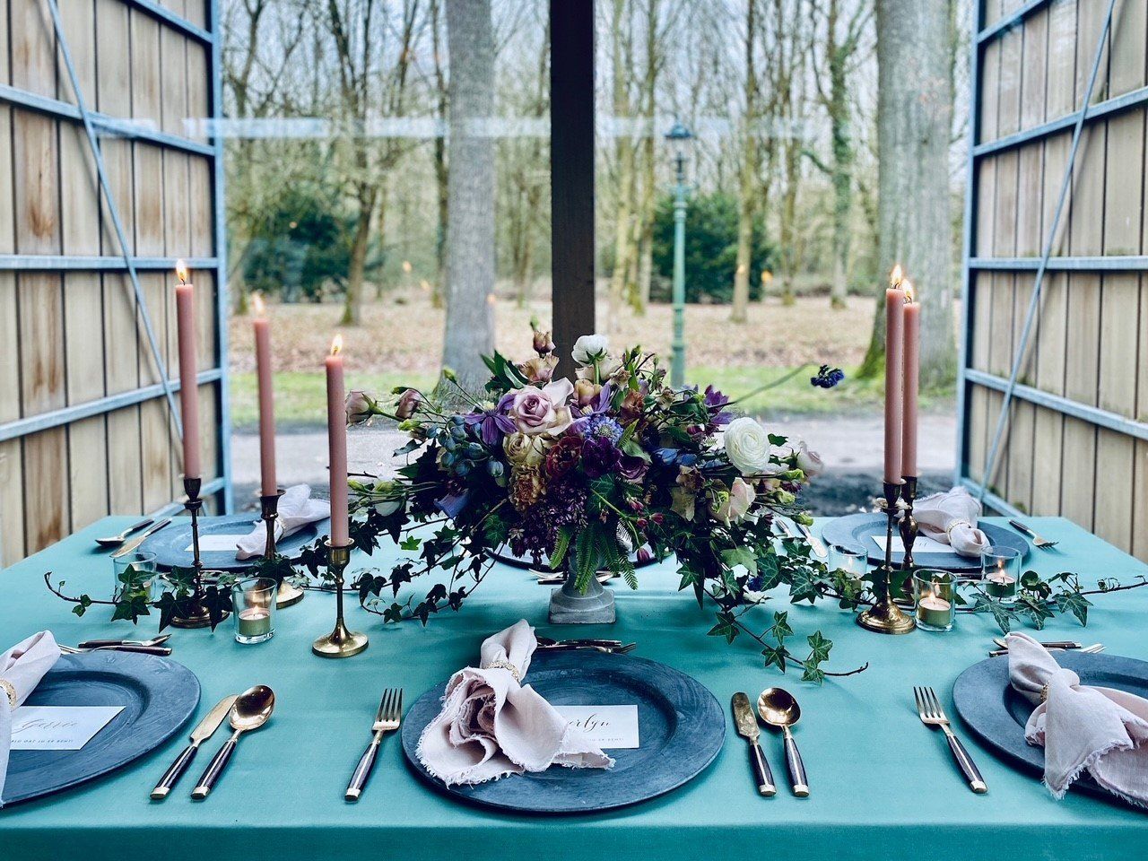 Een tafel met borden, bestek, kaarsen en een vaas met bloemen.