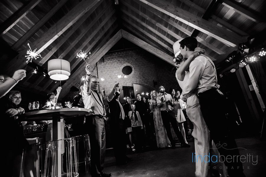 Een zwart-witfoto van een bruid en bruidegom die elkaar kussen op een huwelijksreceptie.