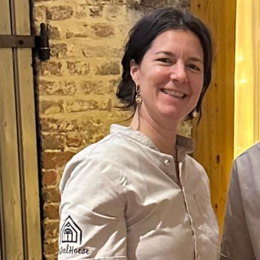 Een vrouw draagt ​​een zwart shirt en een ketting en lacht naar de camera.