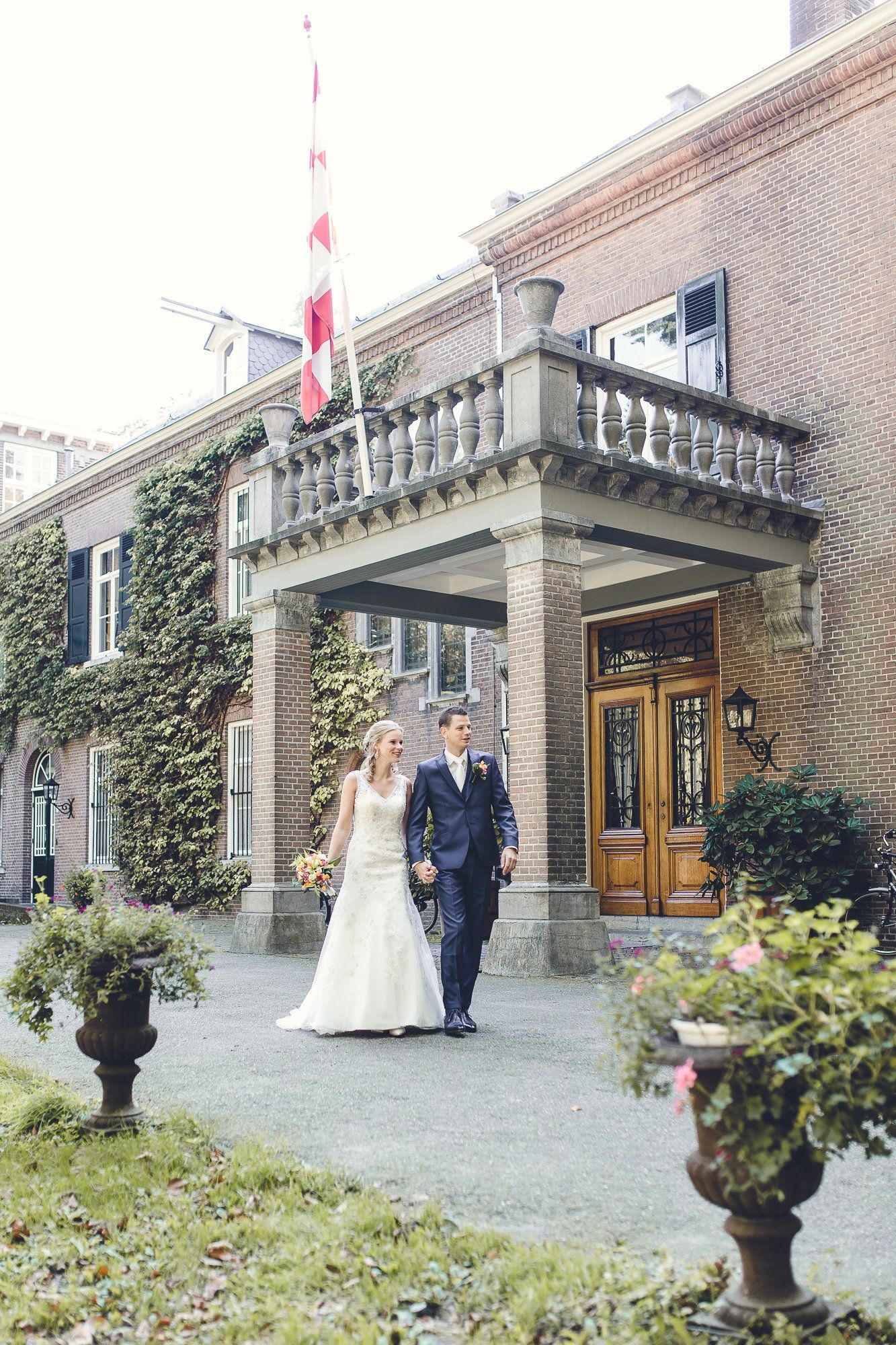 Een bruid en bruidegom lopen voor een groot gebouw.