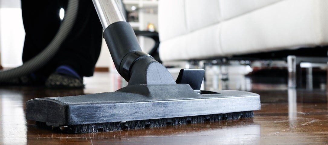 A person is using a vacuum cleaner to clean a wooden floor.