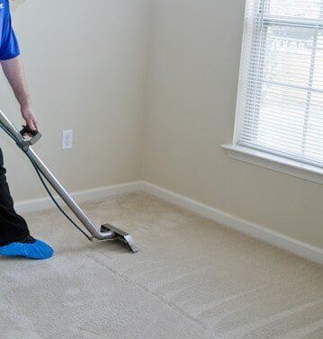 A man is using a vacuum cleaner to clean a carpet in a room.