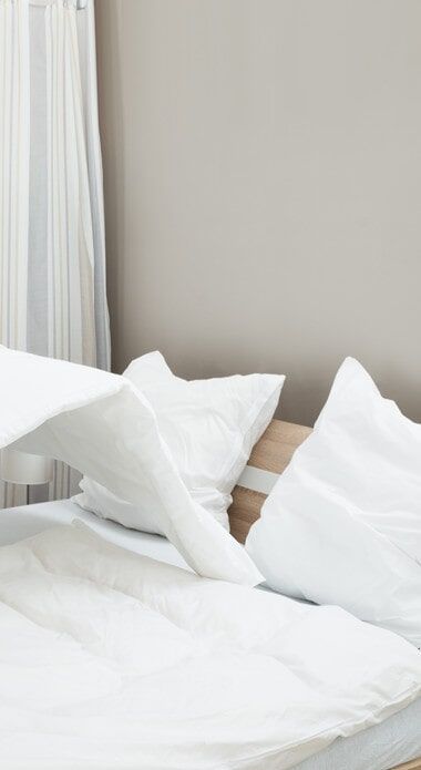 A bed with white sheets and pillows in a bedroom.