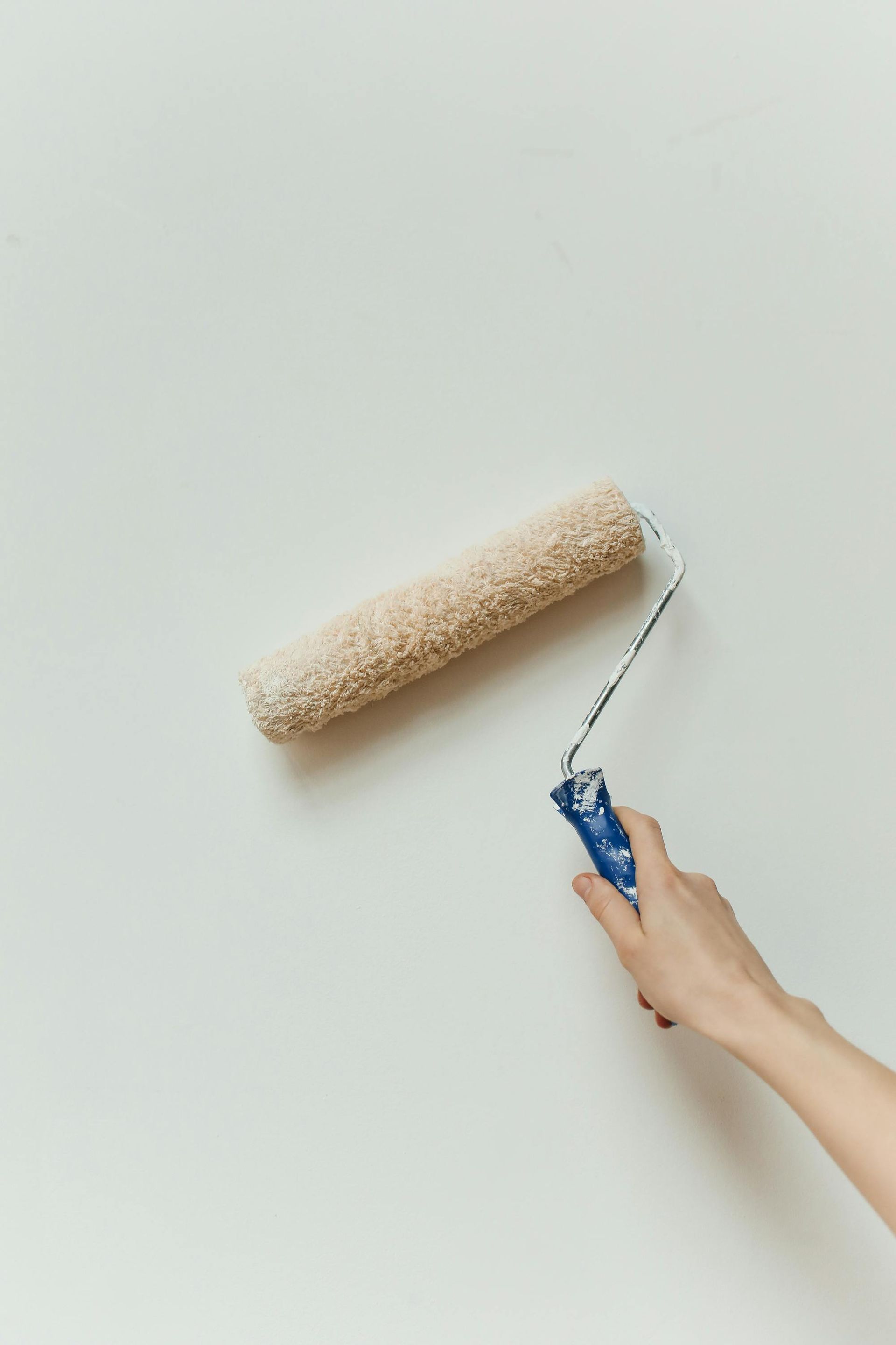 Hand painting a white wall with a paint roller, blue handle, beige roller.