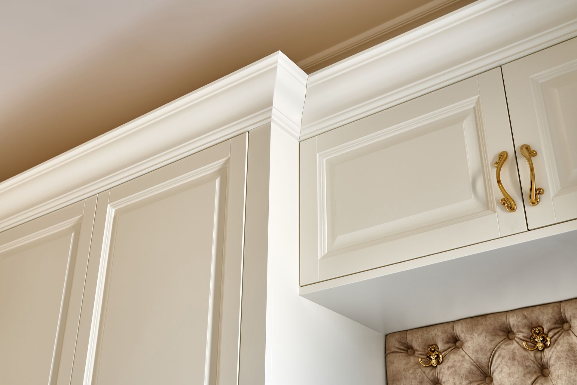Cream-colored cabinetry with decorative trim and gold handles against a white wall.