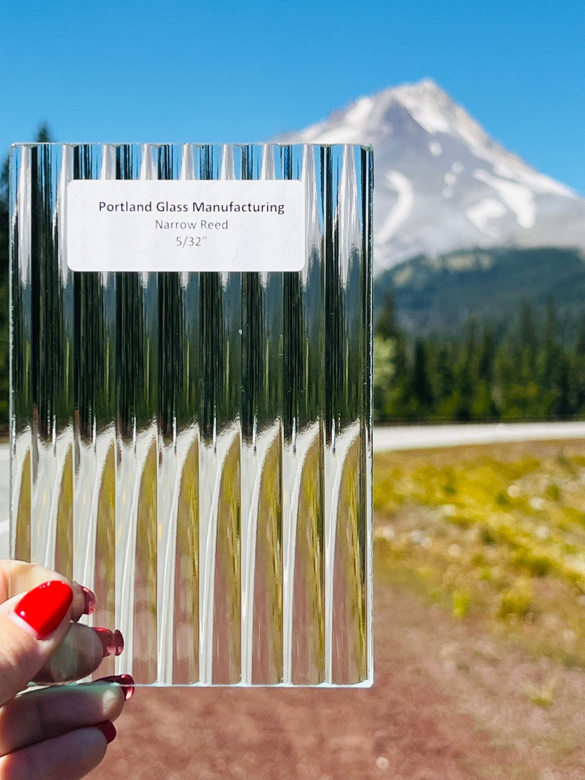 A person is holding a piece of glass with a mountain in the background