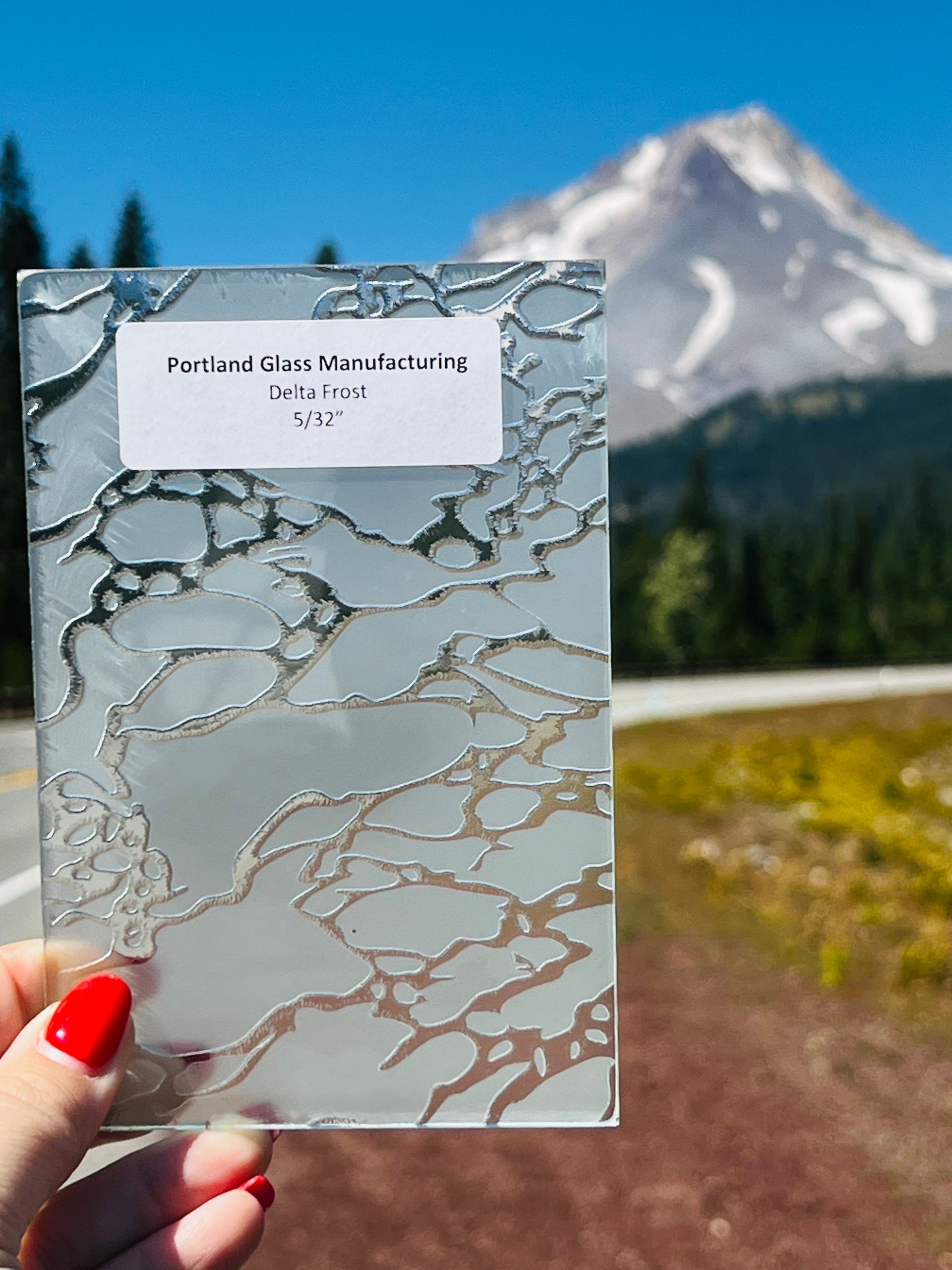 A person is holding a piece of glass in front of a mountain.